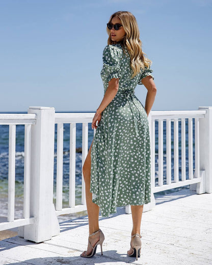 Woman in a green floral dress standing on a deck by the sea