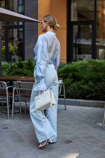 Woman in light blue outfit walking outdoors with a white handbag.