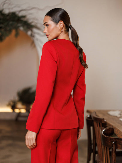 Woman wearing a red suit standing in an indoor setting with wooden furniture and plants.