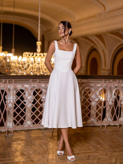 Woman in a white dress standing in an elegant indoor setting with chandeliers.