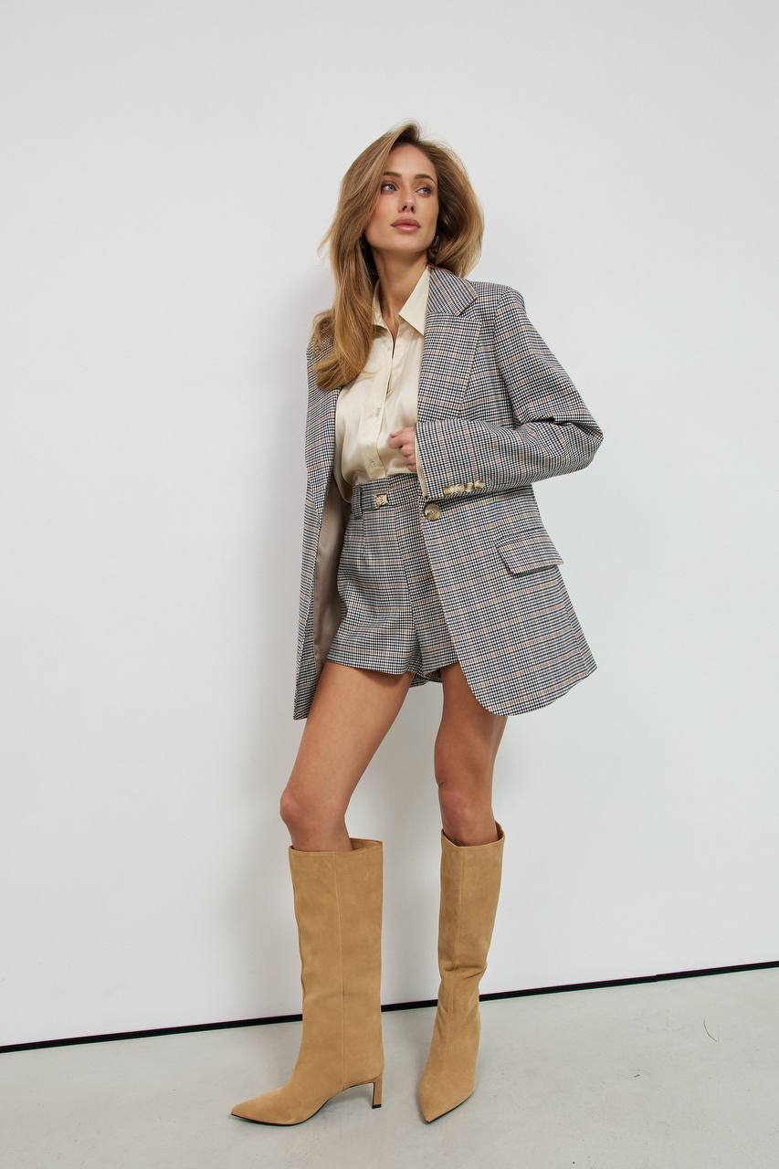 Woman wearing a gray checkered suit with beige knee-high boots against a white background