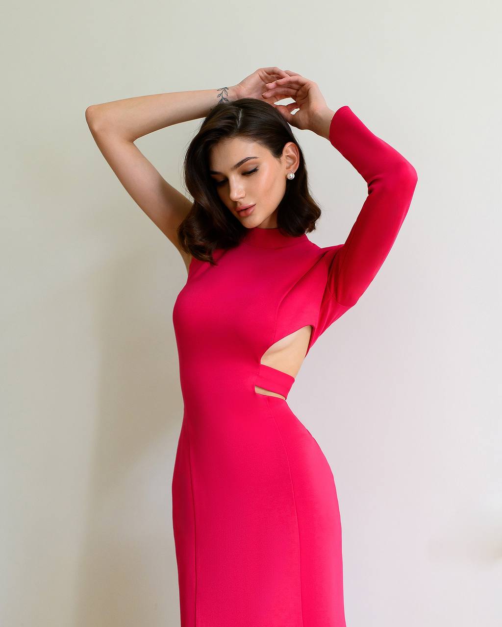 Woman wearing a bright pink dress with cut-out design against a plain background