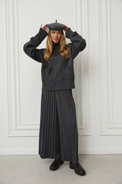 Woman wearing a black outfit with a pleated skirt against a white paneled wall.