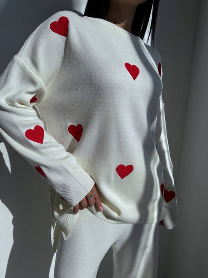 White sweater with red heart patterns worn by a person against a neutral background