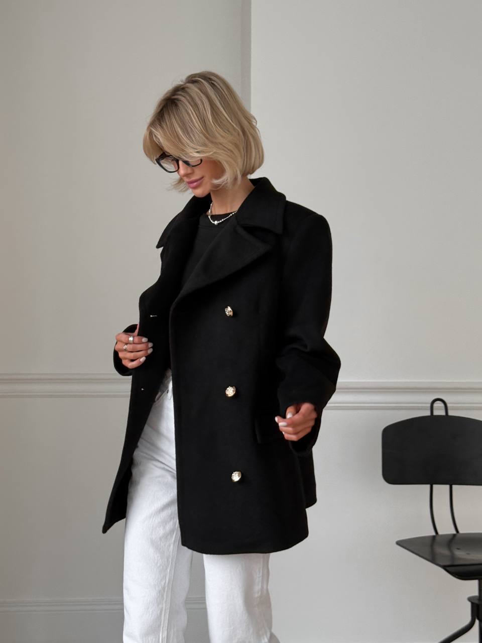 Person wearing a black coat with gold buttons in a minimalistic setting
