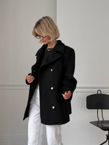 Person wearing a black coat with gold buttons in a minimalistic setting