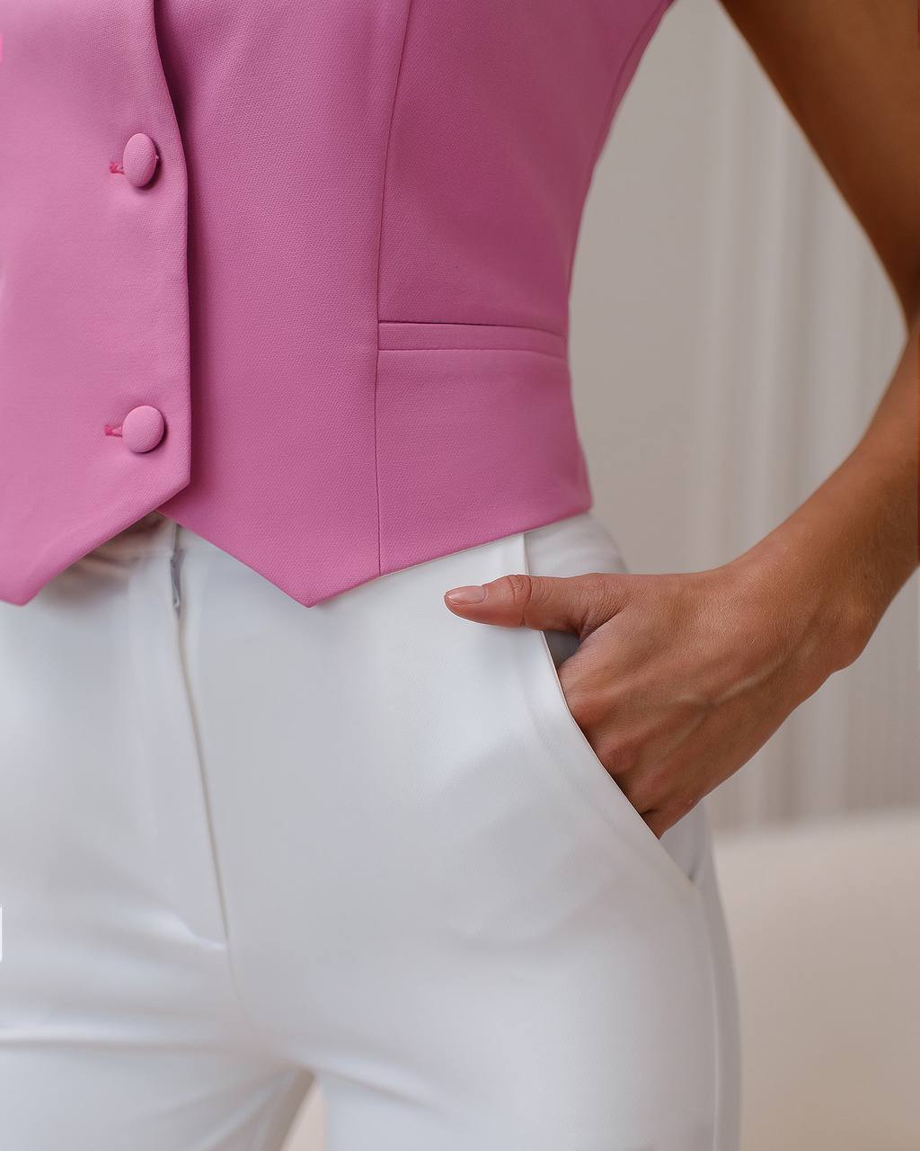 Pink vest with buttons worn over white pants on a neutral background