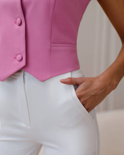 Pink vest with buttons worn over white pants on a neutral background