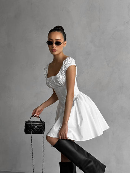 Woman in a white dress holding a black handbag against a gray background