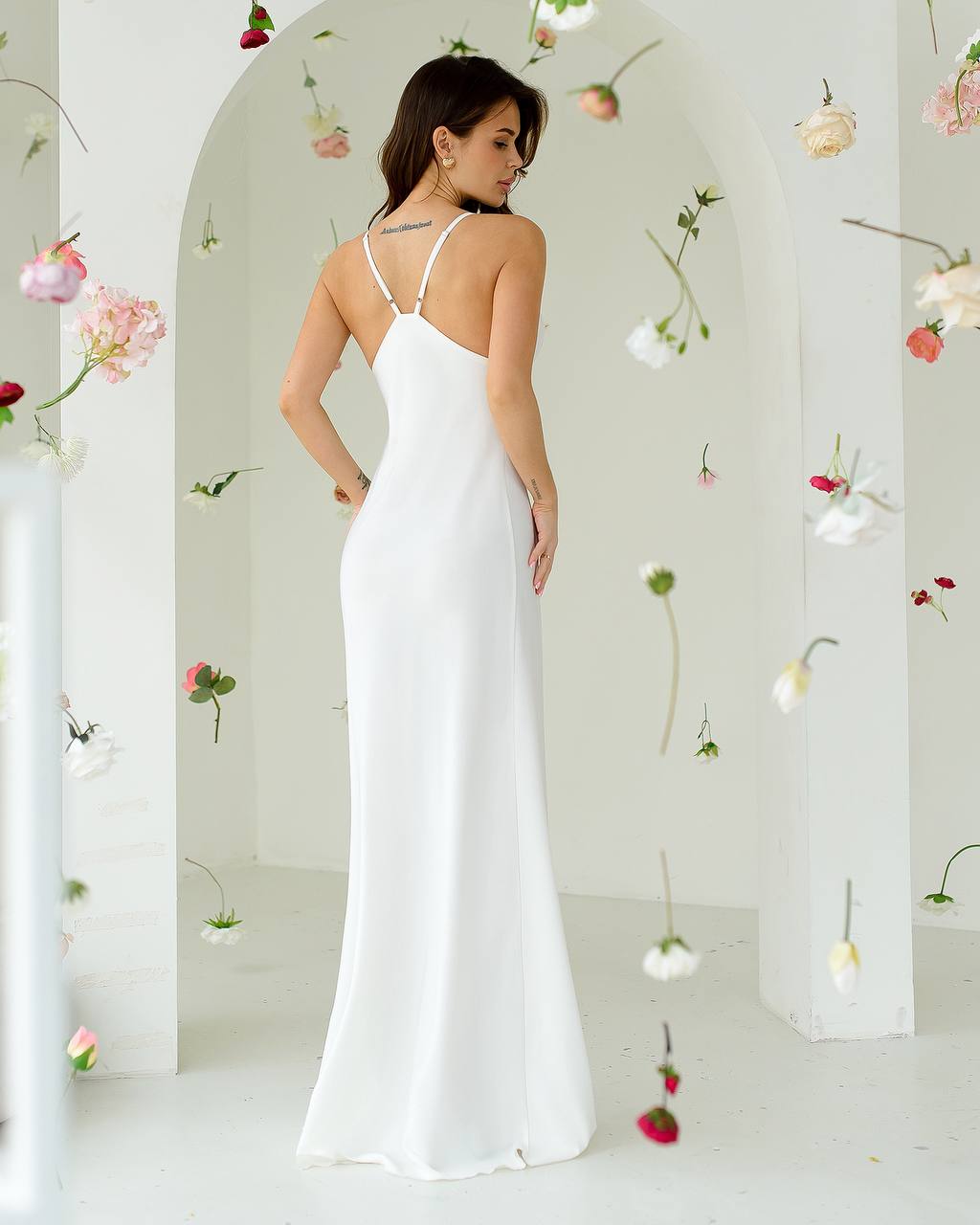 Woman in a white dress standing in a room with hanging flowers