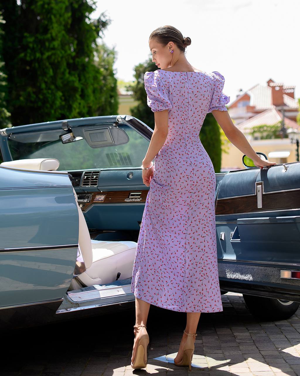 Woman in a purple floral dress standing next to a vintage car