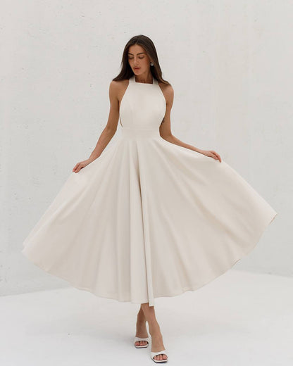 Woman wearing a white halter neck dress against a plain background