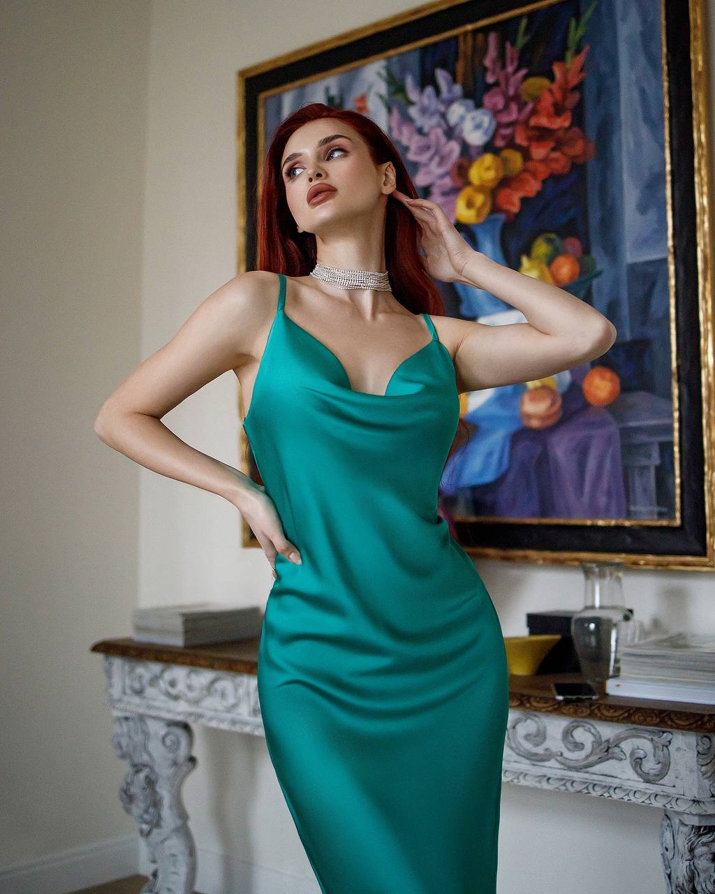 Woman in a teal dress posing in a room with a colorful painting in the background
