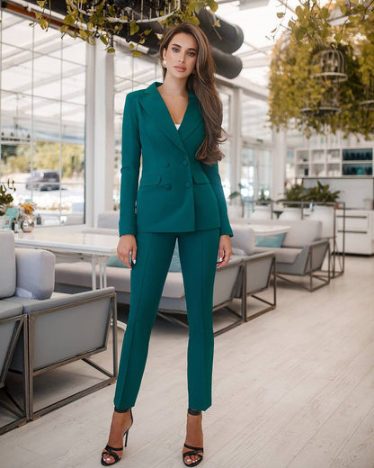 Woman in a teal suit standing in an indoor setting with modern decor.