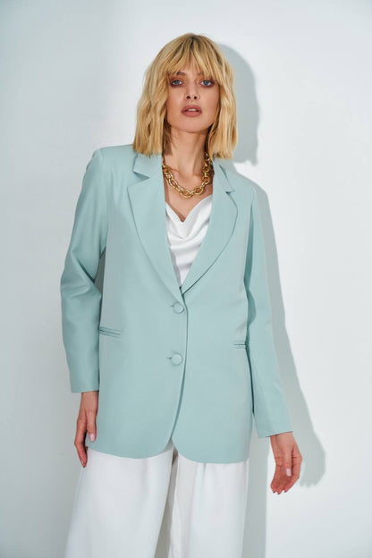 Woman wearing a light blue blazer over a white top and pants on a plain background