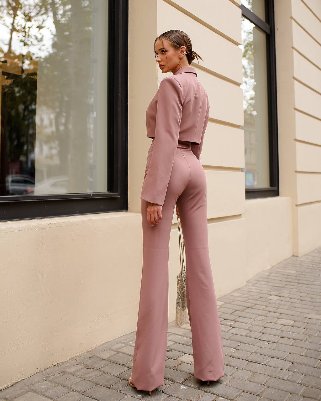 Woman in a pink outfit standing against a beige building.