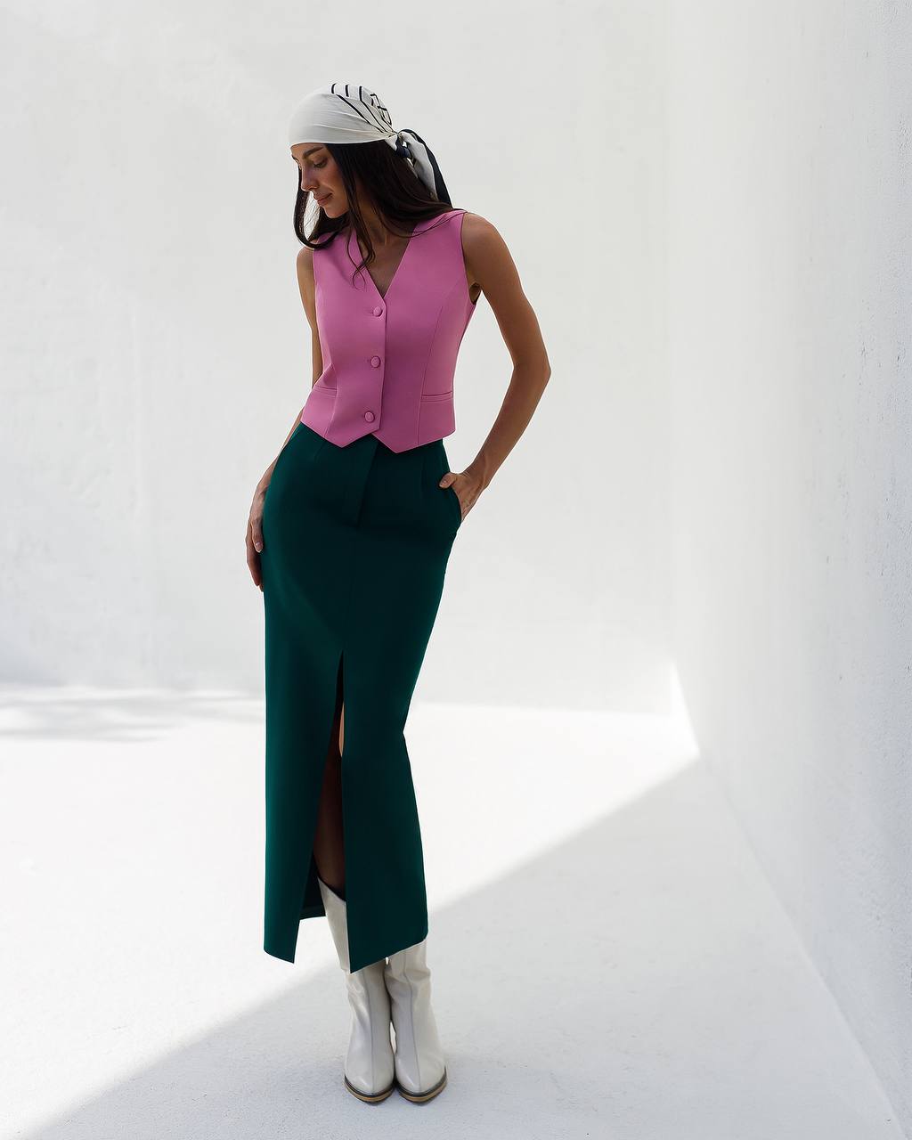 Woman wearing a pink top and green skirt with white boots on a white background