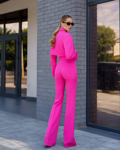 Woman in a bright pink outfit standing against a gray brick wall.