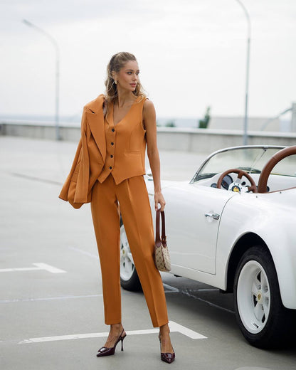 Woman in a mustard yellow suit standing next to a vintage car on a road.