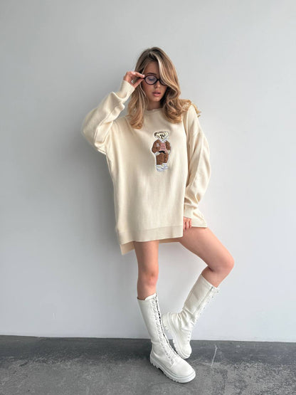 Person wearing a cream-colored oversized sweater and white boots against a plain background