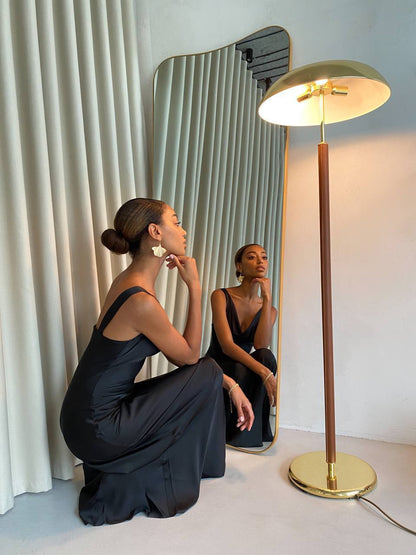 Woman in a black dress sitting on the floor next to a gold floor lamp and mirror.