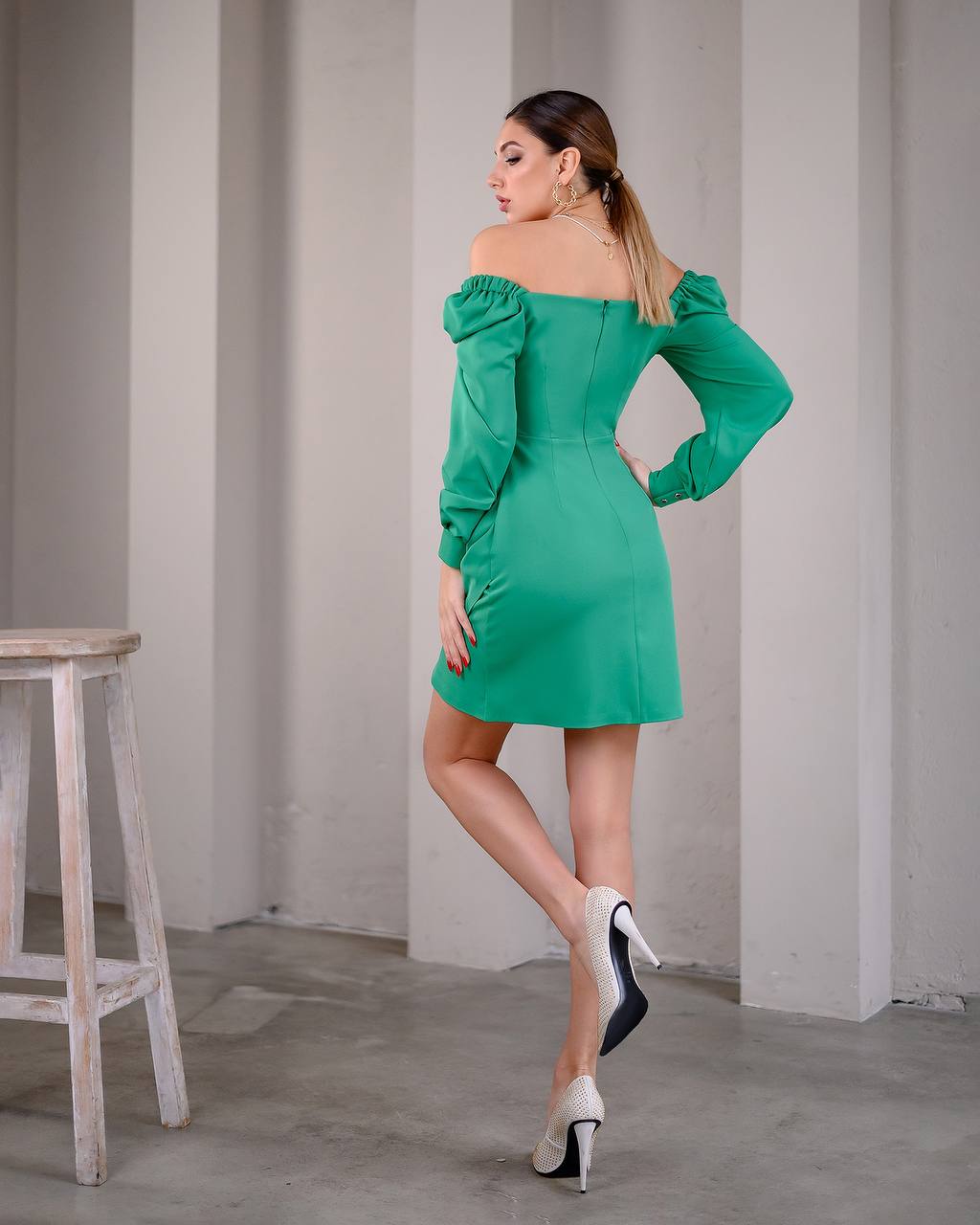 Woman in a green off-shoulder dress posing against a plain wall.
