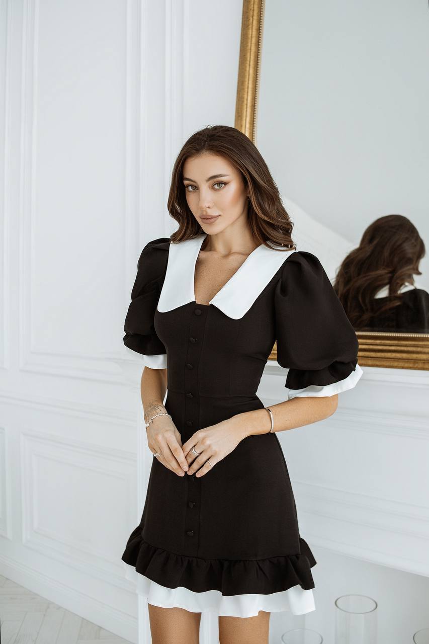 Woman wearing a black dress with white accents standing in front of a mirror.
