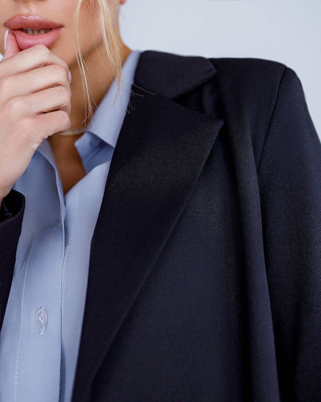 Person wearing a black blazer over a light blue shirt with a blurred background