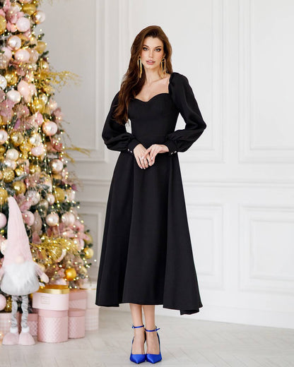 Woman in a black dress standing next to a decorated Christmas tree.