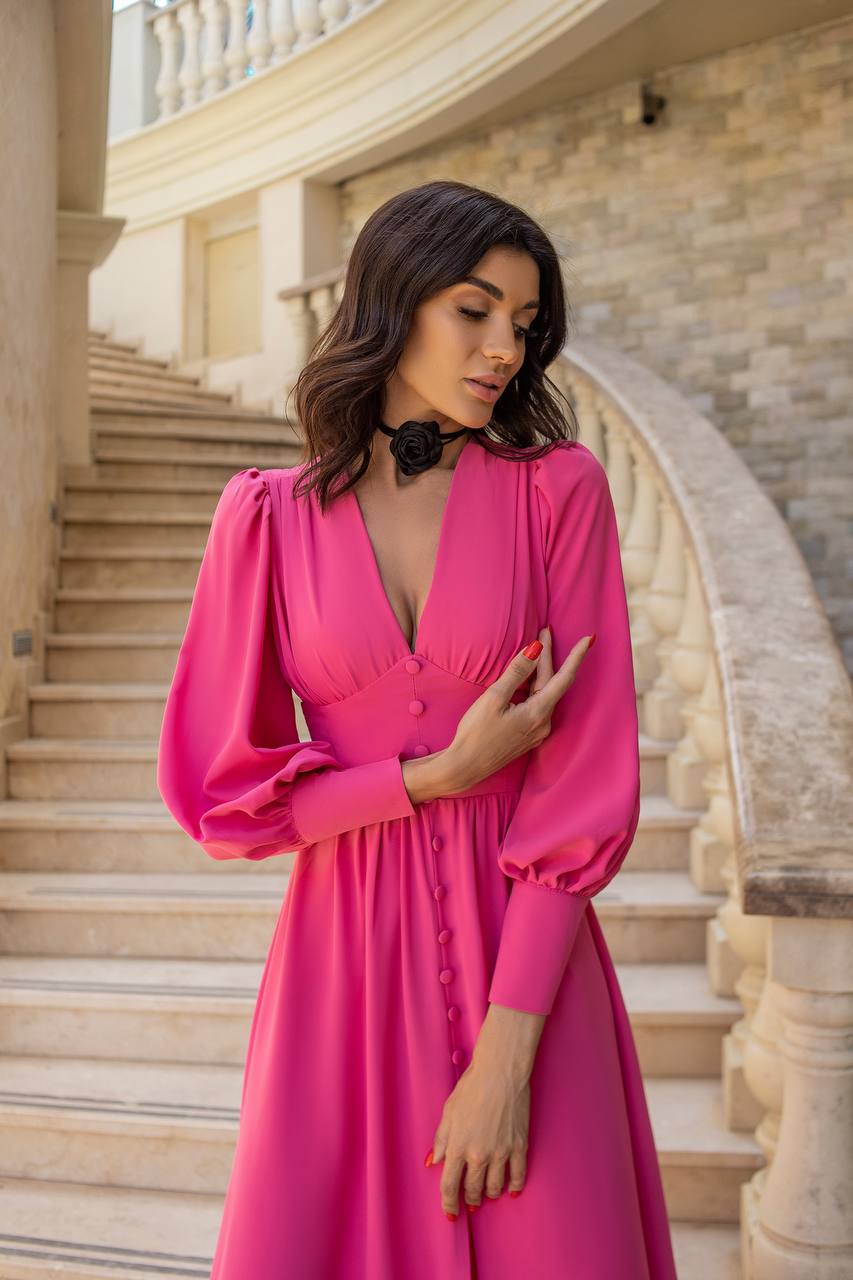 Woman in a pink dress standing on a staircase with stone walls.
