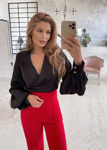 Woman taking a mirror selfie wearing a black top and red pants in a modern room.