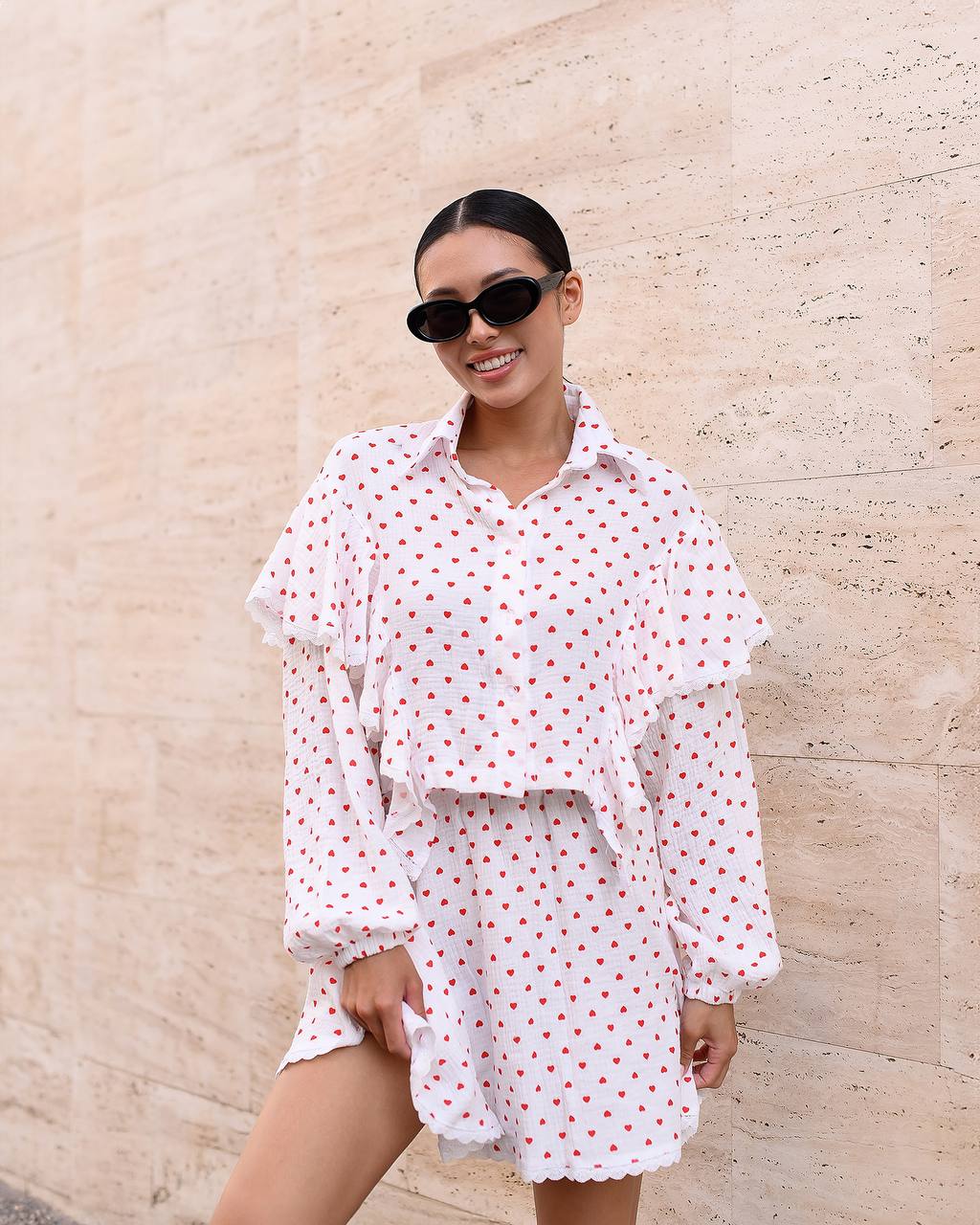 Woman wearing a white polka dot dress with sunglasses against a beige stone wall.