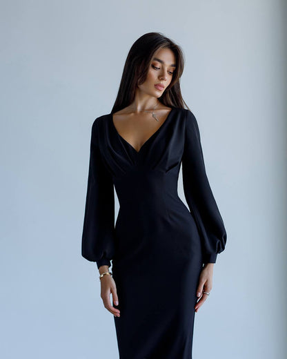 Woman wearing a black dress with long sleeves against a plain background