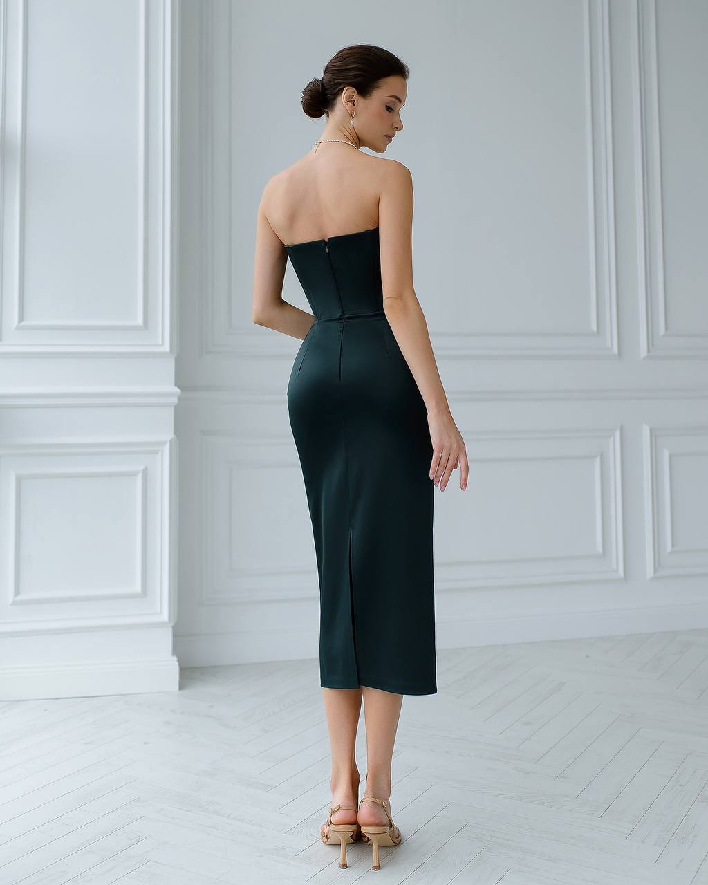 Woman wearing a strapless dark green dress in a white room