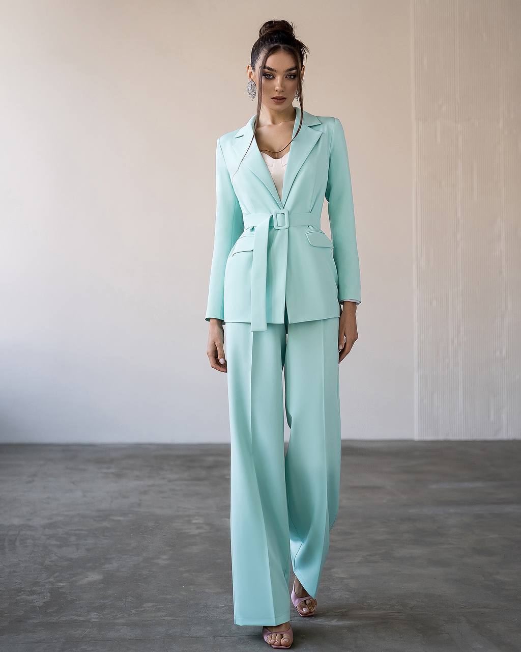 Woman wearing a mint green suit standing against a neutral background