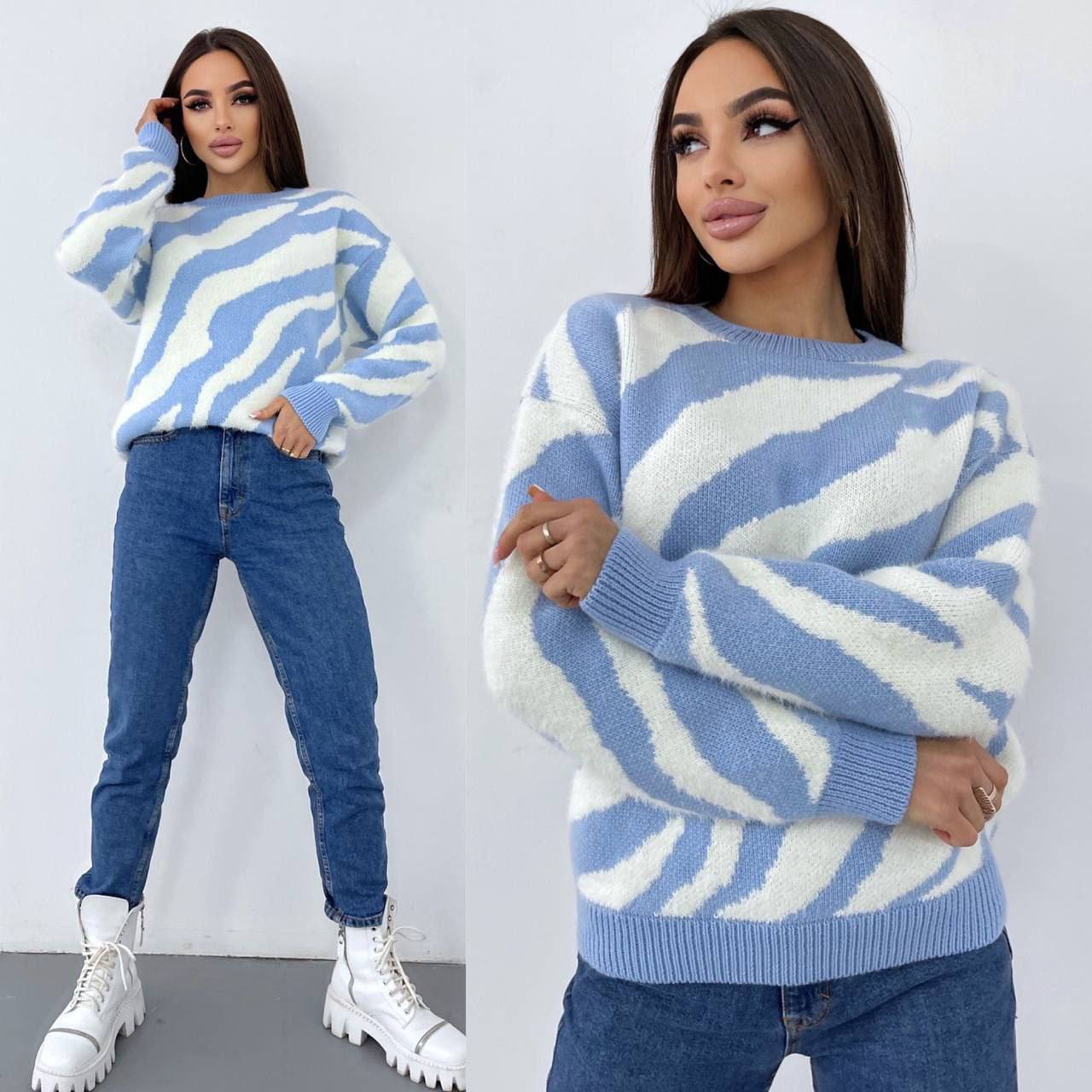Woman wearing a blue and white patterned sweater with jeans and white boots on a plain background