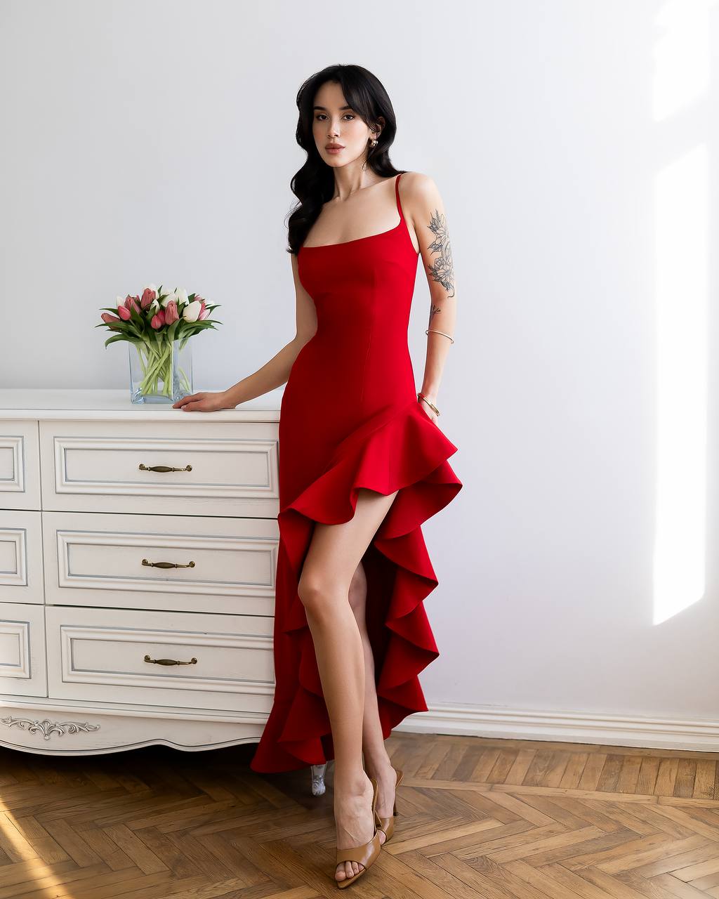 Woman in a red dress standing in a room with a white dresser and flowers.