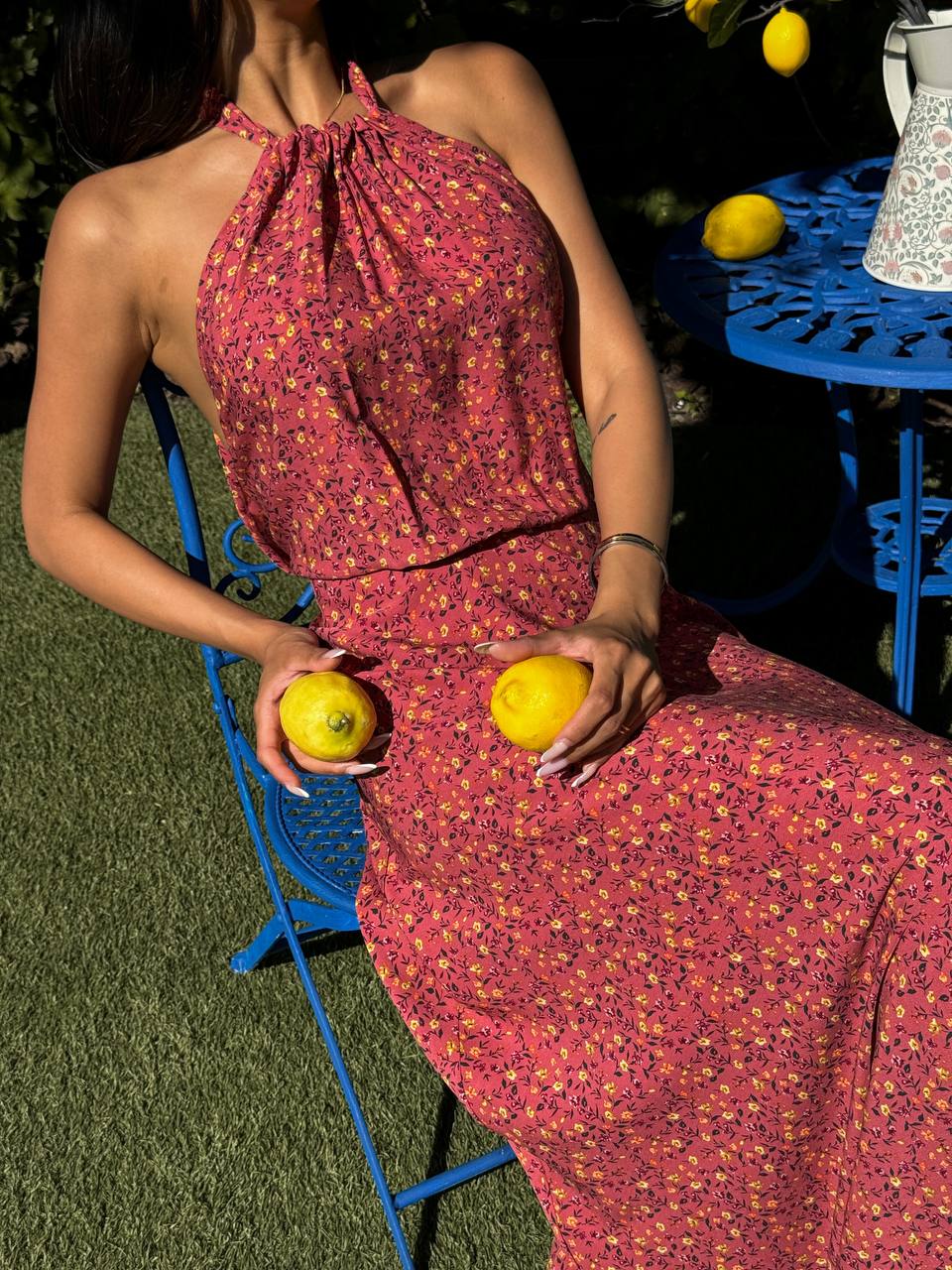 Person wearing a red floral dress holding lemons outdoors.