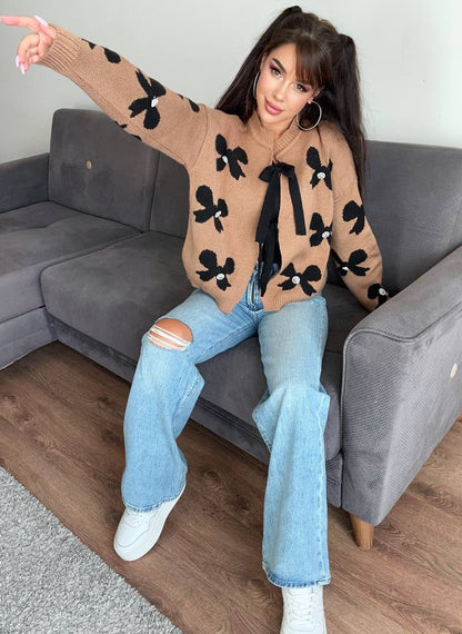 Woman sitting on a gray couch wearing a patterned sweater and jeans.