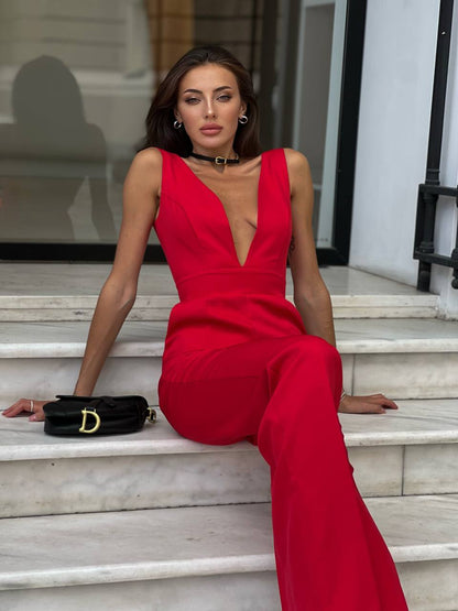 Woman in a red jumpsuit sitting on steps with a black handbag.