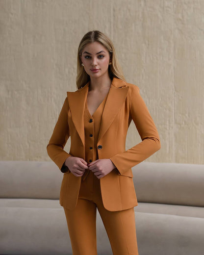 Woman wearing a mustard yellow suit standing against a beige wall.