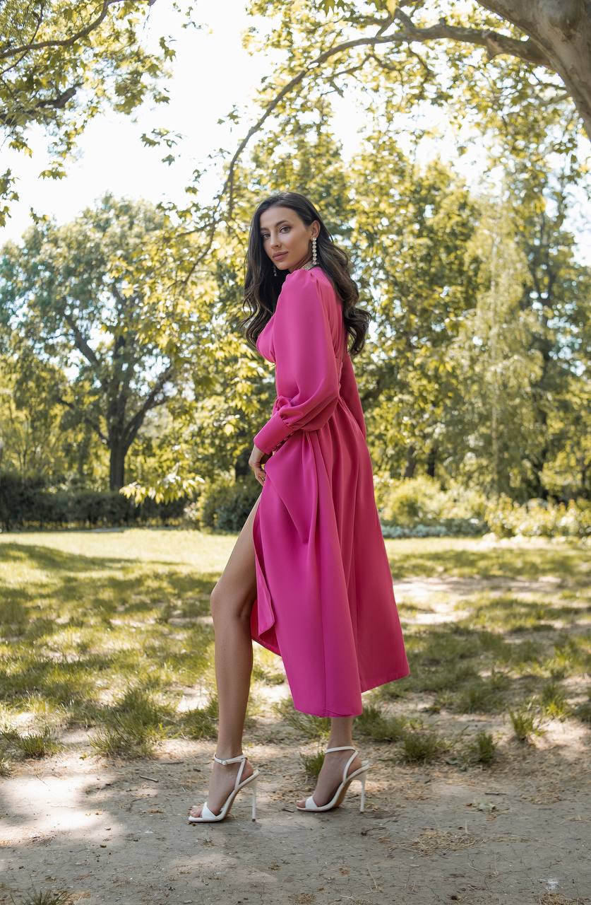 Woman in a pink dress standing in a park with trees and grass in the background