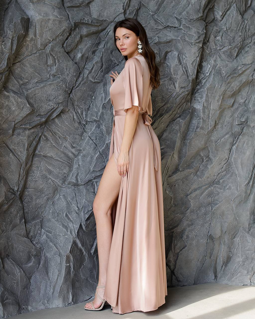 Woman in a long, light pink dress standing against a textured gray wall.
