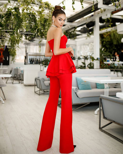 Woman in a red outfit standing in an outdoor setting with greenery and tables.
