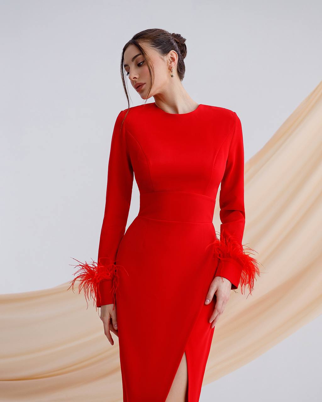 Woman wearing a red dress with feathered cuffs against a plain background