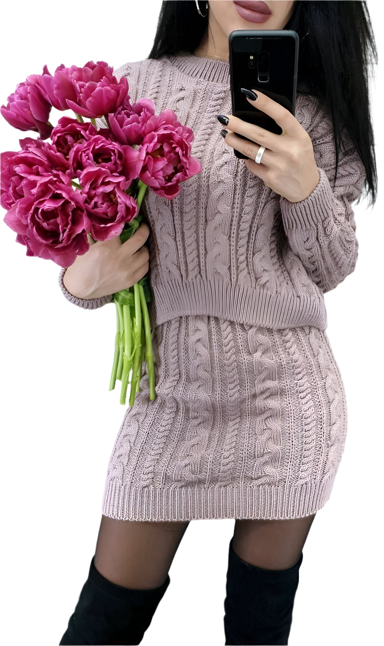 Person wearing a cable knit sweater holding pink flowers and a phone.