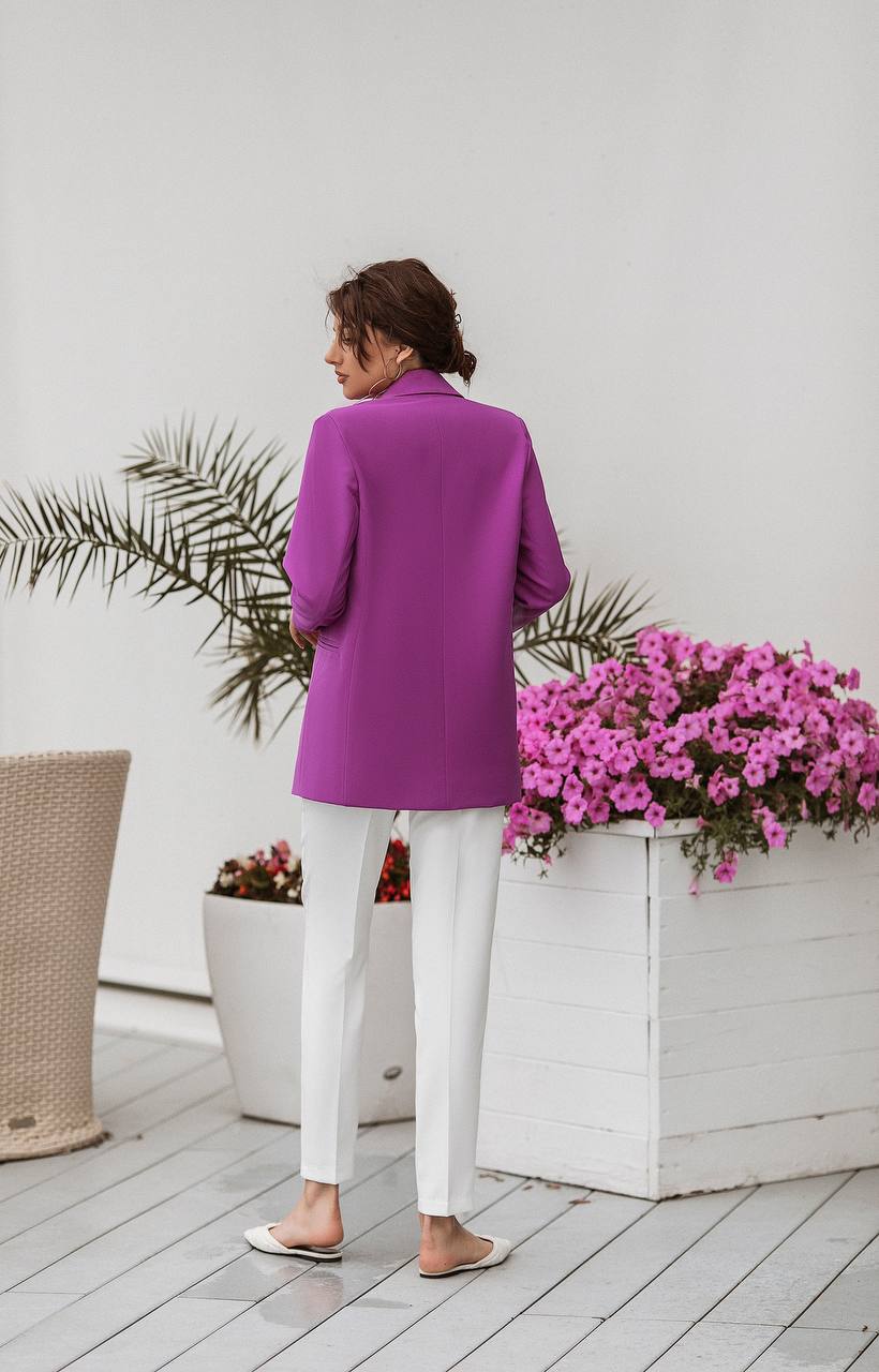 Person wearing a bright purple jacket and white pants standing on a wooden deck with plants and flowers.