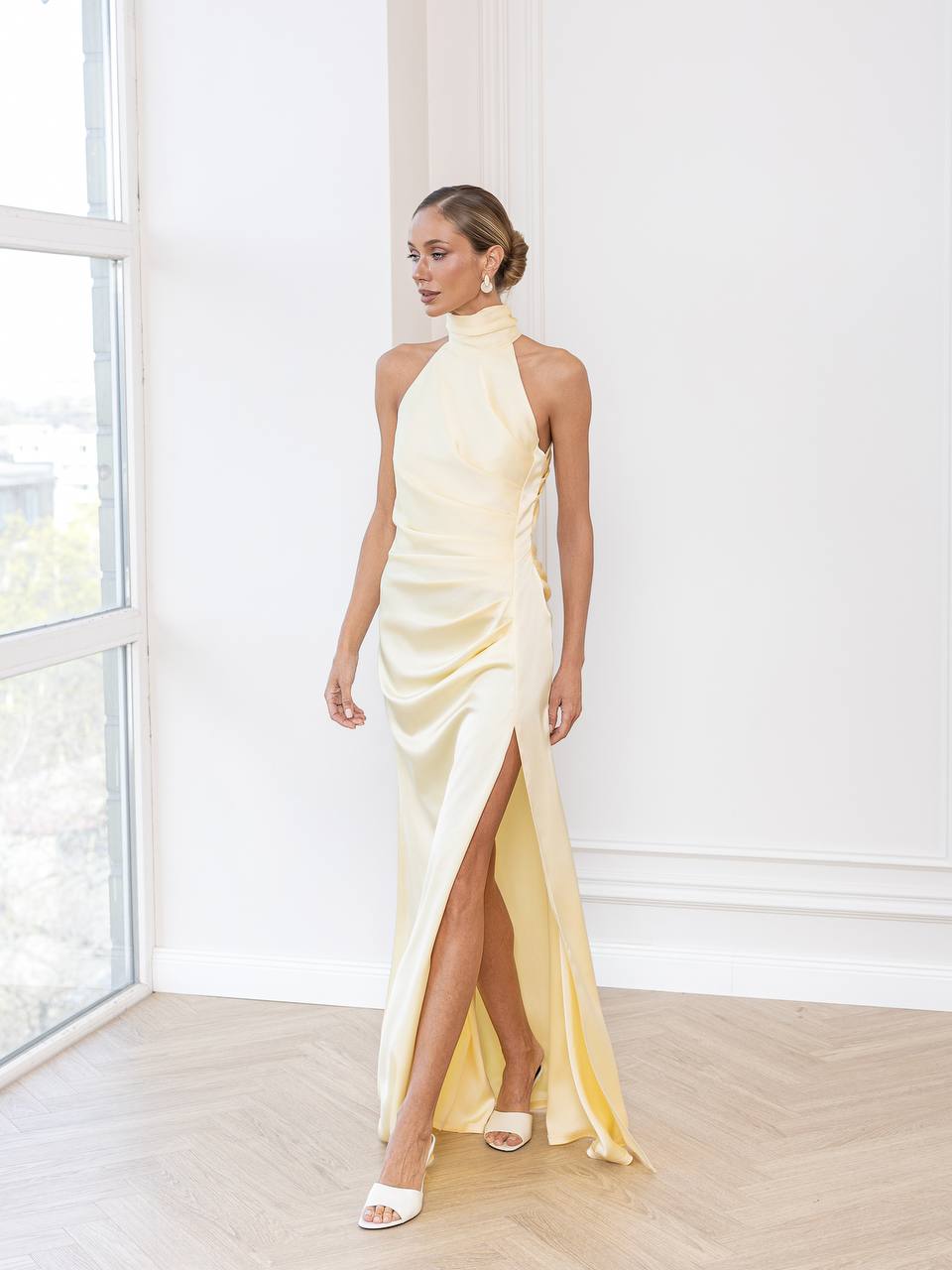 Woman wearing a light yellow evening gown with a high slit in a bright room.