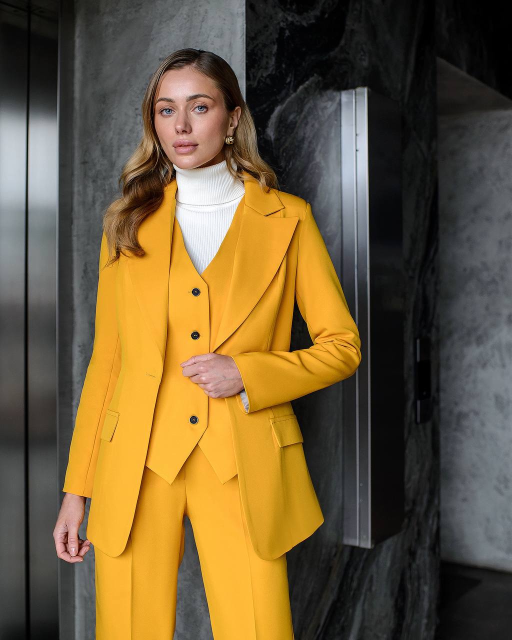 Woman wearing a yellow suit standing against a dark background