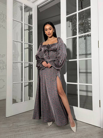 Woman in a long, dark patterned dress standing in a room with large windows.